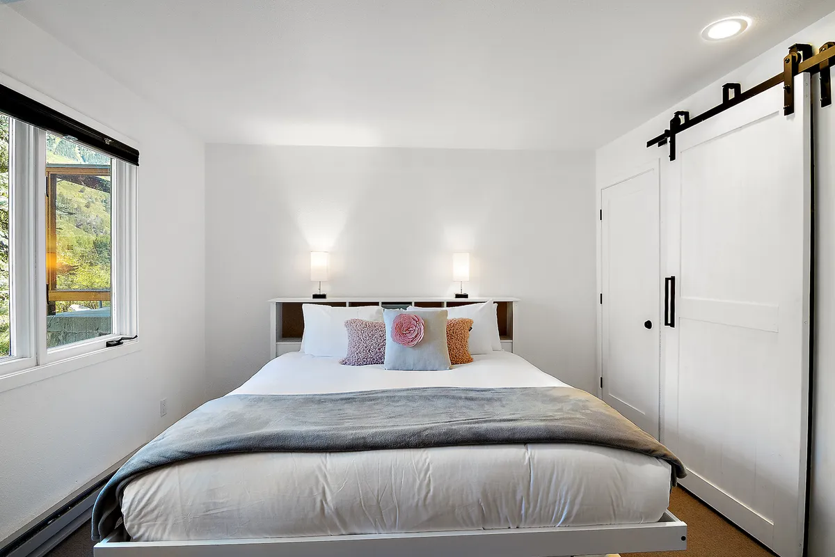 A serene bedroom with a comfortable bed, decorative pillows, nightstands, and a sliding barn door. The ambiance is calm, cozy, and adaptable for various guest needs.