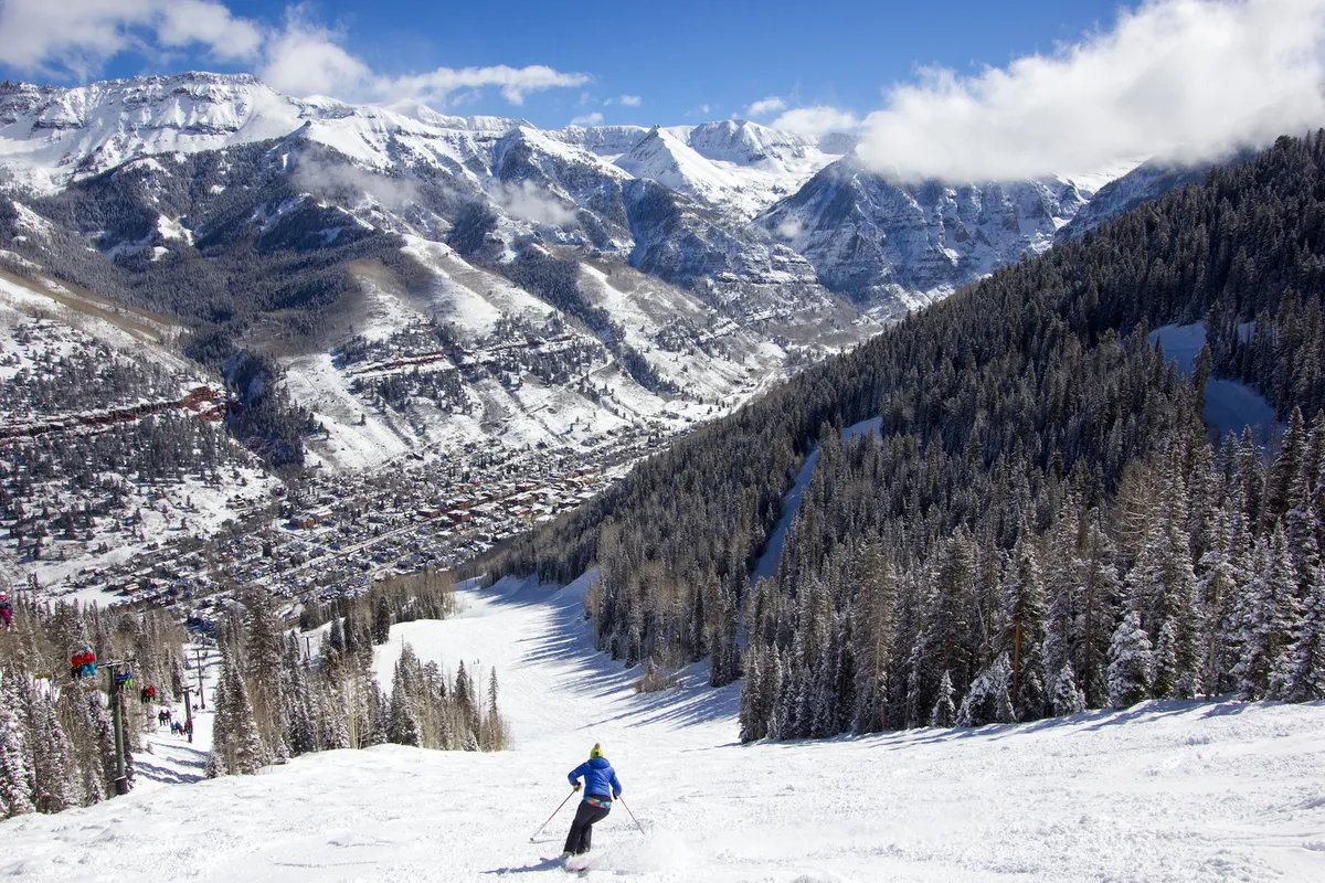 A skier descends a snowy slope with a dramatic mountain range and the town spread out below. The image blends adventure, breathtaking scenery, and proximity to amenities, echoing the section's promise of thrilling outdoor pursuits and a walkable location close to restaurants and shops.