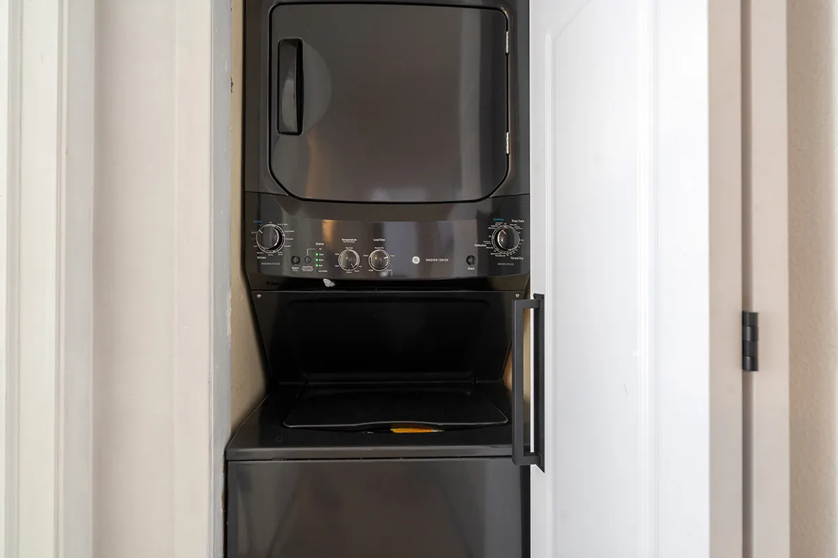 A stacked washer and dryer set neatly enclosed within a modern laundry area, featuring bright lighting and efficient layout. The area appears clean and easily accessible, ideal for families needing in-unit laundry during their stay.