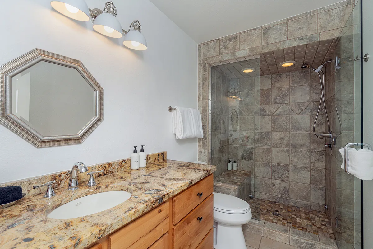 A bright, modern guest bathroom with a granite countertop, mirror with stylish lighting fixtures, and a shower area is shown. The space feels refreshing and well-appointed, ideal for post-adventure refreshment and self-care routines.