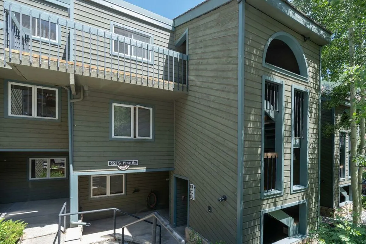 This image showcases the condo's exterior, featuring a balcony, entrance, and large windows with distinctive architectural detailing. The balcony is set up for relaxation or gatherings, and the inviting exterior hints at easy access to nature and community spaces.