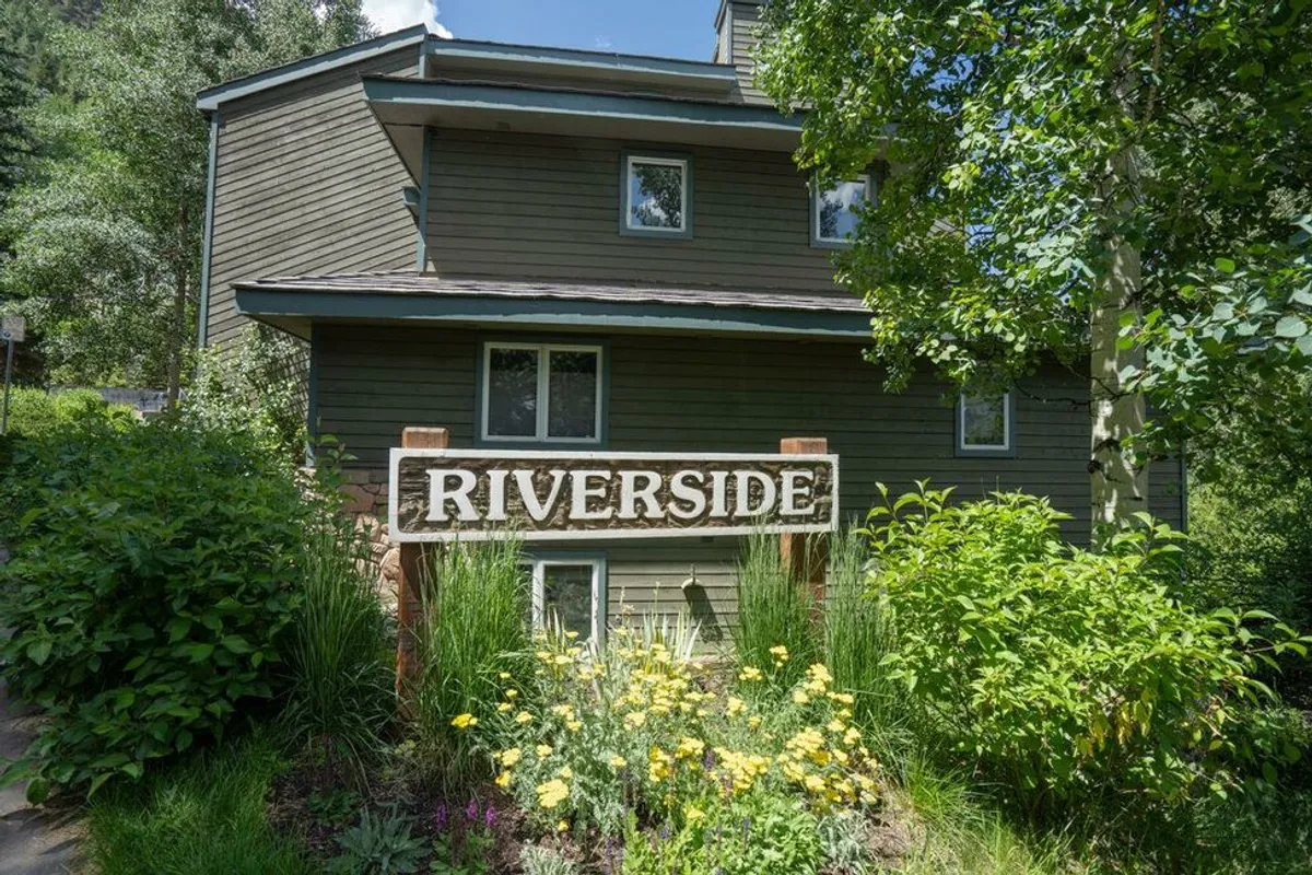 The entrance area marked by a 'Riverside' sign, complemented by a flower garden and the building's facade, creates a welcoming atmosphere and highlights the sense of community.