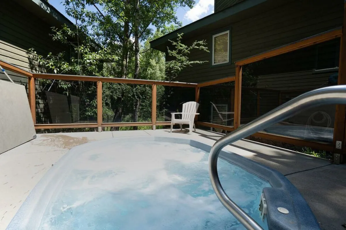 An outdoor hot tub surrounded by lounge chairs and tall trees, offering a tranquil setting with natural views and a sense of privacy. The hot tub area is inviting and hints at relaxation after a day of adventure.