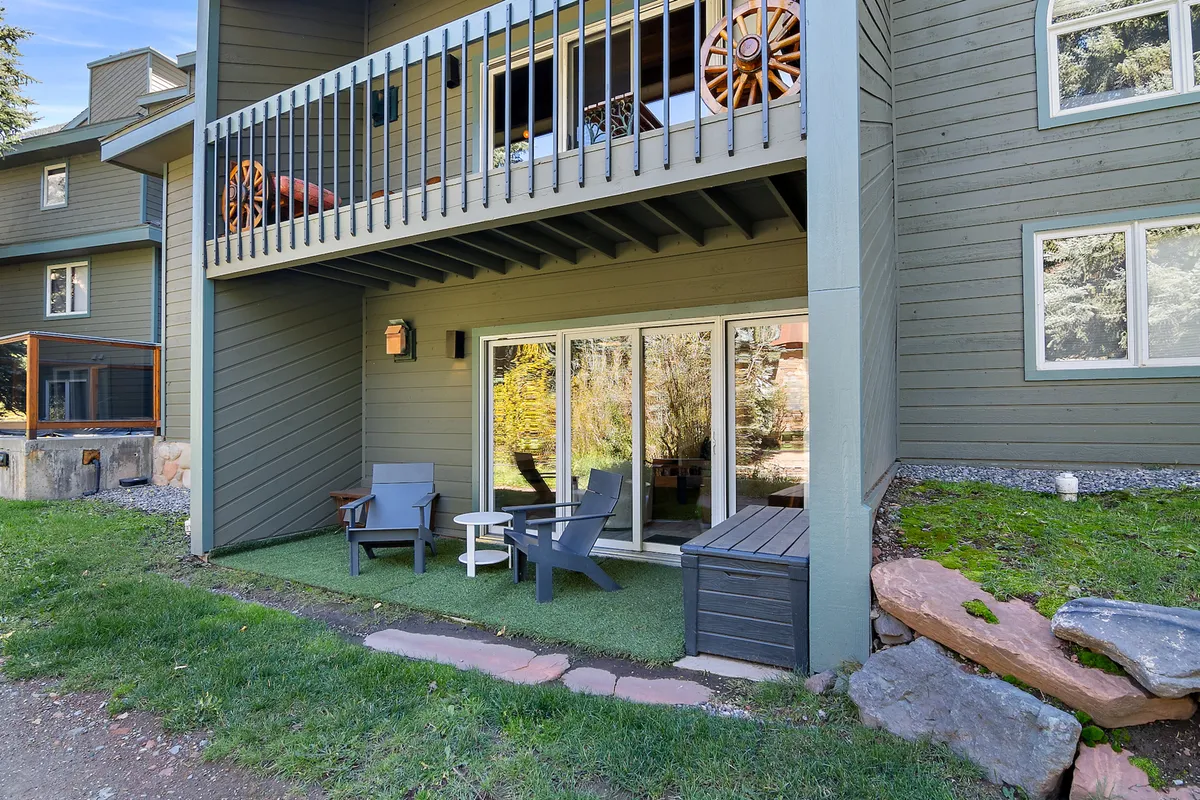 The photo displays a spacious deck just outside sliding glass doors, furnished with deck chairs and an outdoor table, surrounded by greenery. This space offers a seamless transition from the inside to the outdoors, hinting at morning coffees or evening relaxation with river and mountain views.